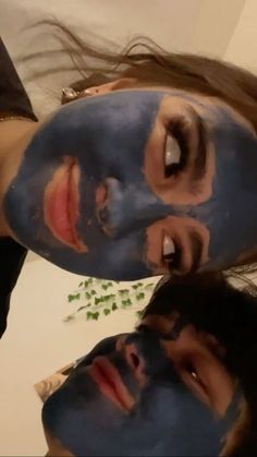 two people with their faces covered in blue clay and green leaves on the table next to each other