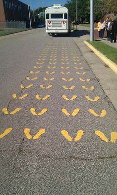 a bus driving down a street next to a sidewalk with yellow footprints on the pavement