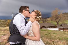 a bride and groom kissing in front of a stormy sky