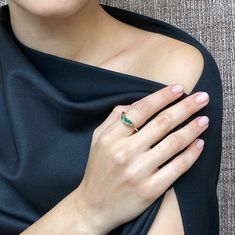 a woman wearing a black dress with a green ring on her left hand and a white diamond in the middle