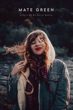 a woman with red hair wearing a denim jacket and scarf, standing in front of a body of water