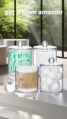 three glass containers with toothbrushes and toothpaste in front of a window