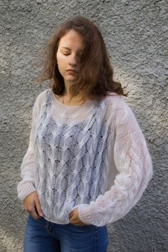 a woman standing in front of a gray wall with her hands on her hips looking down