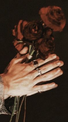 a person holding flowers in their hand with both hands on the other side of them