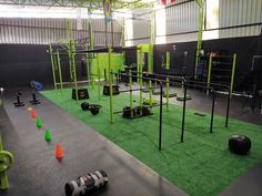 an indoor gym with green grass and black equipment on the floor, surrounded by orange cones