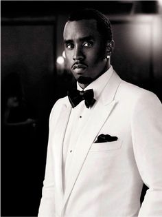 a man in a tuxedo standing next to a perfume bottle