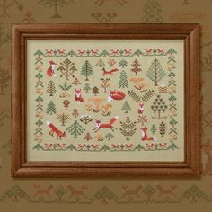 a cross - stitch pattern with animals and trees in the background, framed by a wooden frame