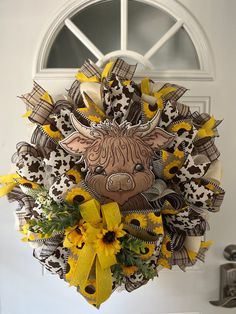 a wreath with a cow and sunflowers hanging from the front door to welcome guests