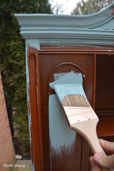 a person holding a paint brush in front of a wooden cabinet with blue paint on it