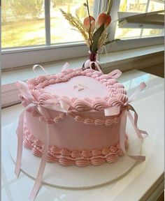 a pink cake sitting on top of a white table next to a window with flowers in it