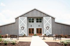 a large gray barn with benches in front of it and flowers on the ground outside