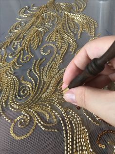 a woman is working on an embroidered fabric with gold sequins and black crochet