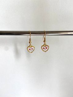 These stunning earrings are the perfect accessory to complete any outfit, and they are sure to make you look and feel your very best! Each earring features two delicate, real pressed flowers preserved in clear resin inside of a small, gold heart charm. You can choose from 24k gold plated wire (comes with rubber earring back), 24k gold plated leverback (huggies), or clip on earrings (no piercing needed). If you would like a combination of flower colors, please specify in the personalization box w White Metal Heart Earrings, Pierced, White Metal Pierced Heart Earrings, White Metal Heart Earrings, White Dainty Earrings With Heart Charm, White Dainty Heart Earrings For Pierced Ears, Dainty White Heart Earrings For Pierced Ears, Dainty Metal Earrings For Valentine's Day, White Metal Heart Earrings For Gift, White Metal Earrings For Valentine's Day