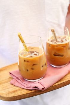 two glasses filled with iced coffee on top of a wooden tray