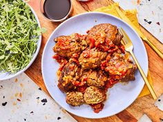 meatballs covered in marinara sauce on a plate next to a bowl of salad