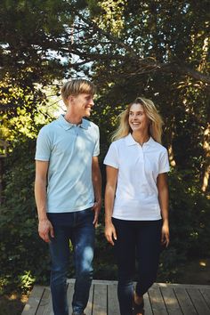 a young man and woman walking on a wooden walkway in front of some trees smiling at each other