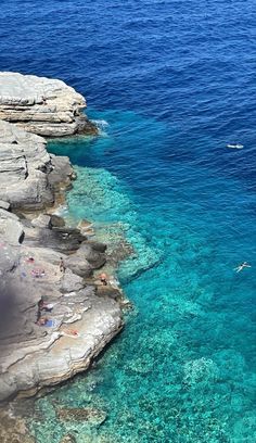 people are swimming in clear blue water near the rocky shorelines and cliffs on an island