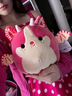 a woman holding a pink stuffed animal in her hands and wearing a pink dress with white polka dots