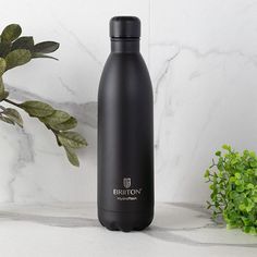 a black water bottle sitting on top of a white counter next to a green plant