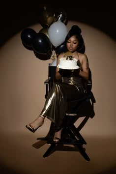 a woman sitting in a chair holding a cake and balloons