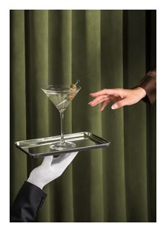 two hands reaching for a martini glass on a tray