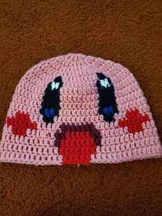 a crocheted pink beanie with black eyes and red hearts on the front