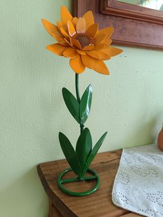 a yellow flower sitting on top of a wooden table next to a green planter