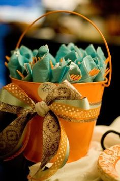 an orange bucket filled with green napkins on top of a table next to cookies