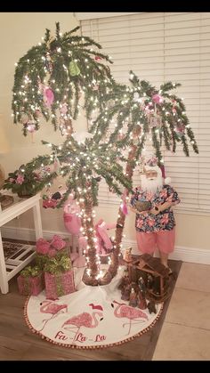 a christmas tree with presents under it and a santa clause in the middle, surrounded by pink flamingos