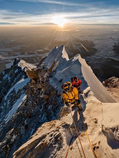 two people climbing up the side of a snow covered mountain