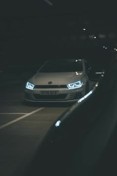 a white car driving down a dark street at night with its headlights turned to the right