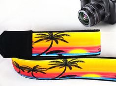 a camera strap with palm trees painted on it and a digital camera next to it