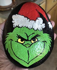 a hand painted rock with the grin face on it, wearing a santa claus hat