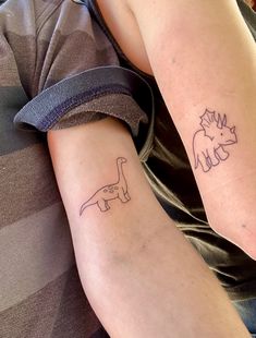 two people with tattoos on their arms, one has a dinosaur and the other has a bird