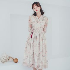 a woman standing next to a white wall wearing a dress with floral print on it