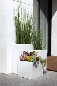 two white planters with plants in them sitting on the ground next to a building