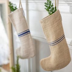 two christmas stockings hanging from hooks on the wall next to a fireplace with greenery