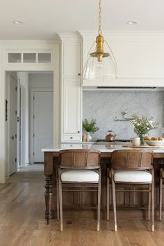 a kitchen with white walls and wooden floors has an island table surrounded by wicker chairs