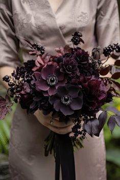 a woman holding a bouquet of purple flowers in her hands and wearing an elegant dress