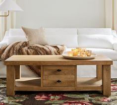 a coffee table with candles on it in front of a white couch and rugs