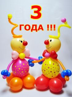 two colorful balloons sitting next to each other on top of a white surface with an orange and yellow balloon in the shape of a clown