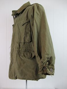 "Vintage 1940s WWII U.S. Army military M-1943 field jacket. Made of green cotton. Has chinstrap, button front, four pockets, shoulder epaulets and drawstring at the waist. Size 34R. Size small/medium. Actual measurements are: 42\" at the chest 40\" at the waist 18.5\" shoulder seam to shoulder seam 21\" shoulder seam to cuff 30\" overall length In wrecked condition. Has small spots of tar, paint, some cracked and replaced buttons. Wear hole at collar." Olive Military Cotton Utility Jacket, Olive Cotton Military Utility Jacket, Olive Cotton Military Style Utility Jacket, Military Style Olive Cotton Outerwear, Olive Military Cotton Outerwear, Military Style Cotton Parka With Flap Pockets, Vintage Khaki Utility Jacket With Flap Pockets, Vintage Khaki Utility Jacket With Buttons, Vintage Cotton Parka