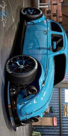 an old blue car hanging from the side of a wall with a tire on it