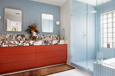 a bathroom with blue tile and red cabinetry in the corner, along with a large mirror on the wall