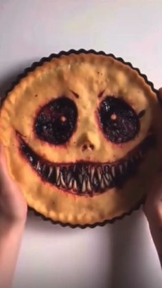 a person holding up a pie with a face painted on it's crusts