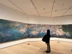 a woman standing in front of a large painting on display at an art gallery with wooden floors and white walls