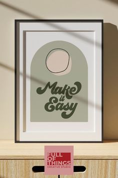 a framed poster with the words make it easy in front of a wooden shelf and shadow