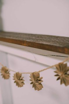 brown paper flowers are hanging from a string on a window sill in front of a white wall