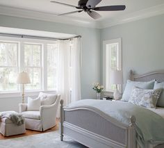 a bedroom with a bed, chair, and ceiling fan in front of two windows