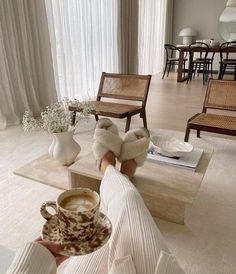 a person holding a coffee cup in their hand while sitting on a couch with two chairs